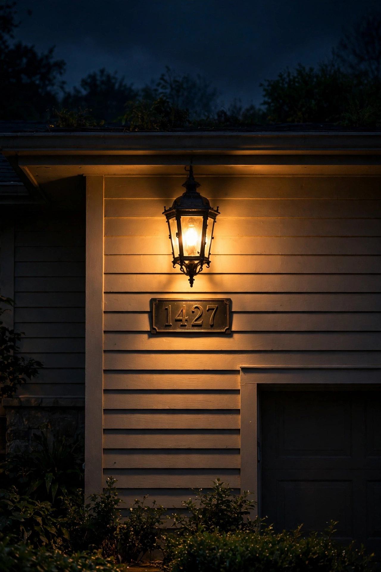 Carriage lantern above an illuminated house number plaque on a garage wall at night