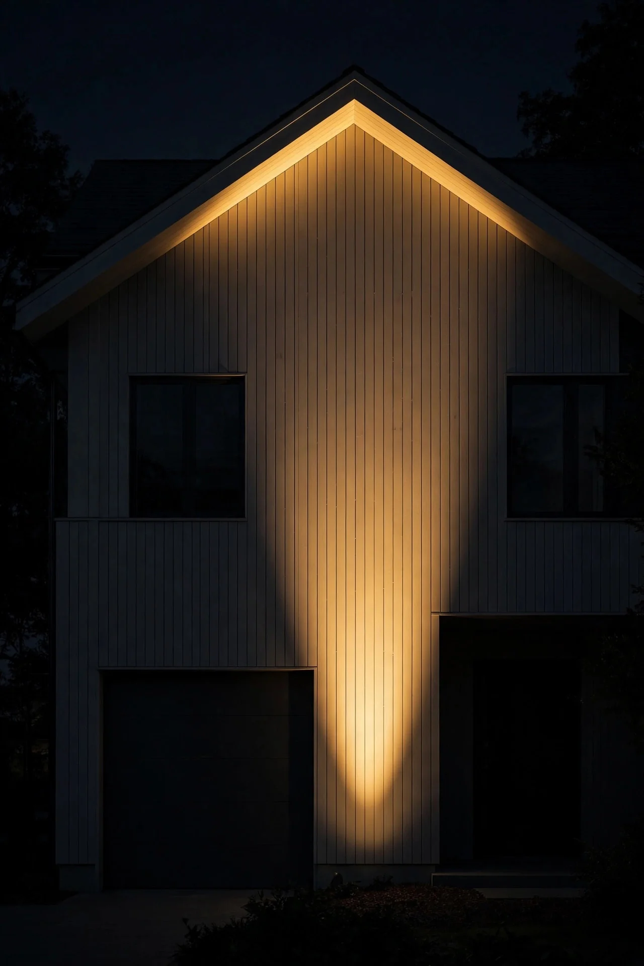 Single warm spotlight washing the front facade of a house in golden light at night